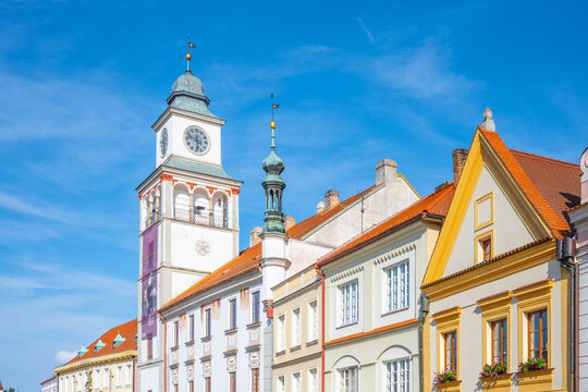 The lookout tower stands tall in the old town hall of Trebon. The sky is clear with few clouds. People walk around, enjoying the architecture of the buildings nearby.