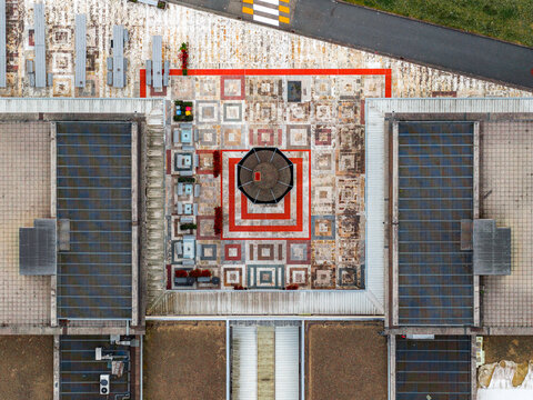 Aerial view of a geometric courtyard with a central octagonal structure, surrounded by modern building rooftops and paved areas in Leccio, Toscana, Italy.