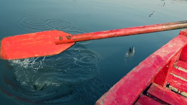 Wooden oar rowing a red boat on calm river water in India