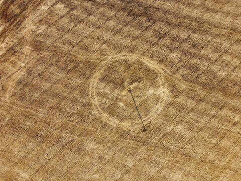 Aerial view of a crop circle in a golden wheat field near Wymington, showing distinct circular patterns in the dry soil in Rushden, England, United Kingdom.