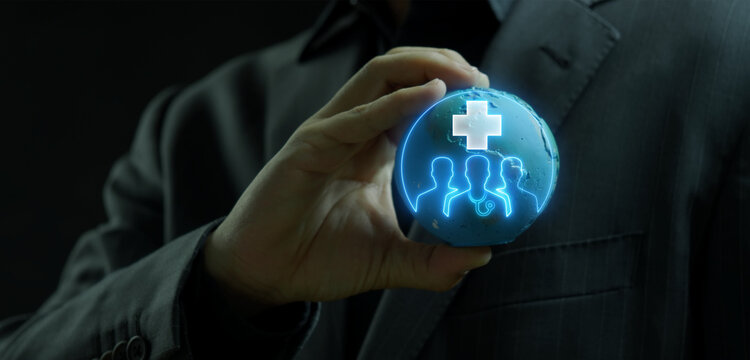 Businessman holding world globe model displaying glowing medical cross symbol over team profile avatars overlay. Global healthcare insurance network and international employee wellness concept.
