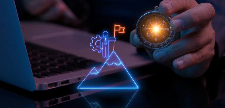 Businessman using laptop computer while holding glowing magnetic compass guiding mountain summit flag milestone. Strategic navigation direction and business milestone goal achievement concept.