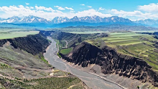 Aerial view of a winding braided river flowing through a deep rocky canyon under a clear blue sky in Anjihai Grand Canyon, Xinjiang, China