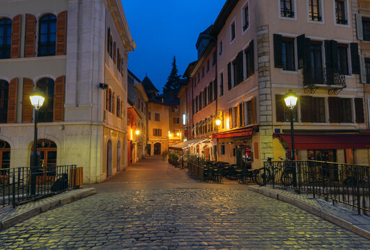 Cobblestone street with historic buildings and glowing street lamps in Annecy, France, during blue hour.