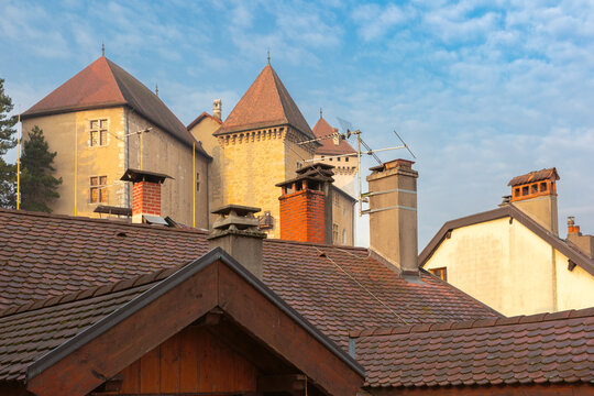 Stone towers rise above traditional red tiled rooftops and chimneys in Annecy, France.
