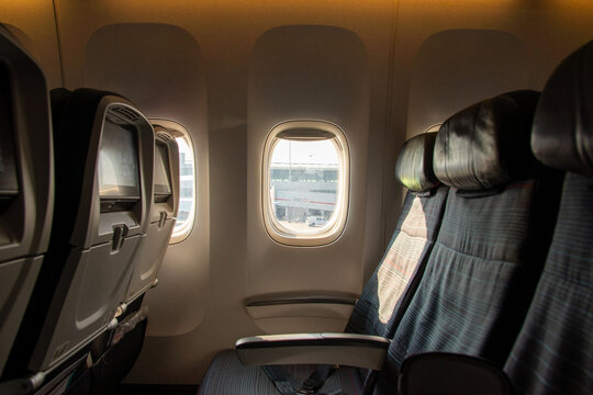 Row of empty airplane seats beside a sunlit cabin window