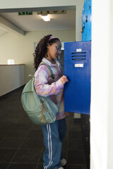 African American teenage girl opening blue locker in school hall wearing pale fleece and green pack © wavebreak3