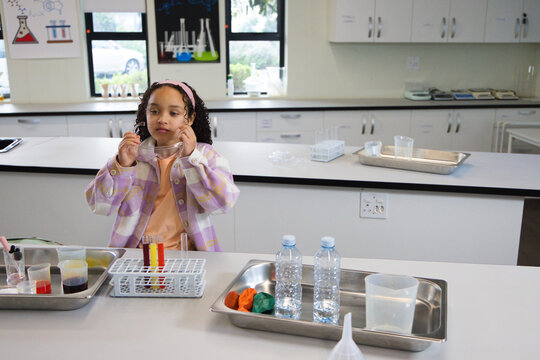 African American female child studying at lab bench, wearing pastel jacket and holding goggles