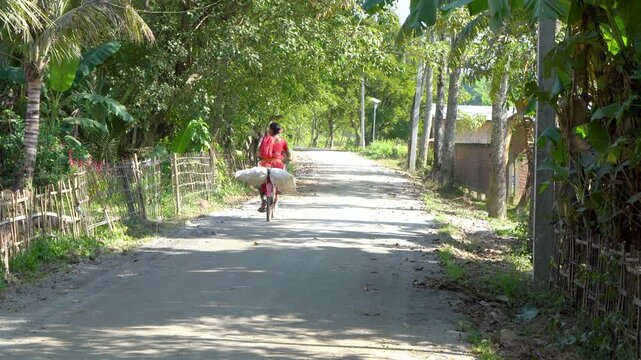 Villager Cycling Rural Road with Sacks, Assam