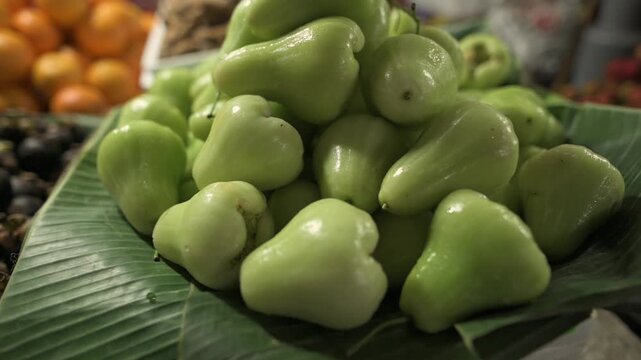Vivid Green Wax Apples Displayed. Colorful Array Of Pale Green Fruits At Busy Market Stall. Vibrant Wax Apples Arranged Neatly On Banana Leaves In Lively Street Market Setting