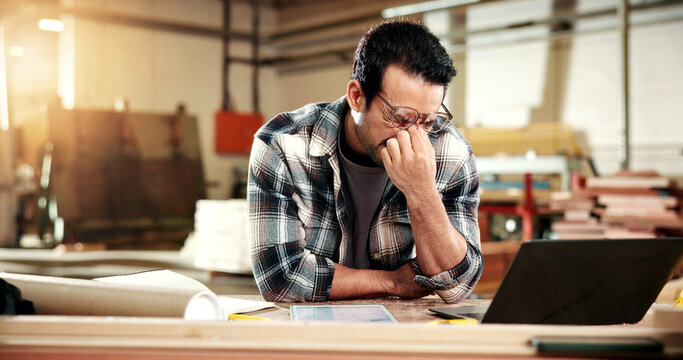 Man, carpenter and glasses with eye strain in warehouse for wood production fail or freight delay. Frustrated, male person or carpentry mistake with stress or laptop for bad news on delivery schedule