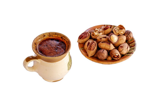 a rustic ceramic cup of freshly brewed coffee with a rich layer of crema alongside a small ceramic dish filled with whole and shelled pecan, macadamia and walnut nuts