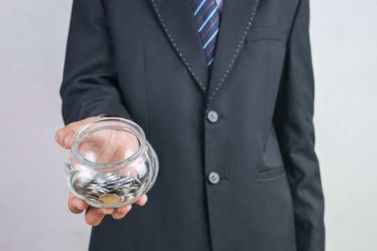 Closeup of Businessman Extending Hand with Coin Filled Glass Jar
