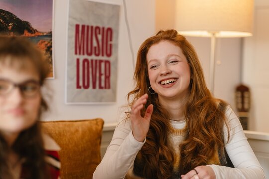 Two teenage girls smiling and talking while chatting in a comfortable bedroom