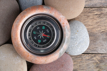 Navigation compass in marble bowl with smooth river stones on wooden background, top view macro. © freeman83