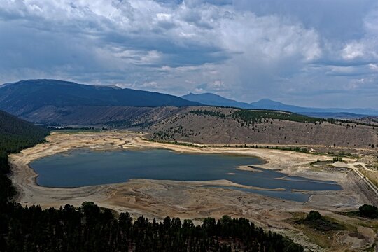 Aerial view of Clear Creek Reservoir with low water levels and exposed shoreline, surrounded by pine forests and mountains in Chaffee County, Colorado, United States.