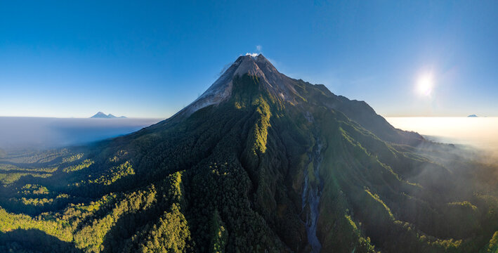Aerial view of the majestic Mount Merapi volcano with lush green slopes and volcanic crater under a clear blue sky in Cangkringan, Special Region of Yogyakarta, Indonesia.