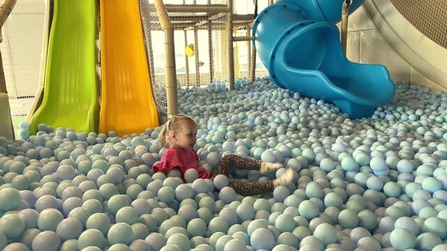 Little girl moving through a colorful indoor ball pit at a play center, childhood fun, active play, family entertainment, joyful activity.