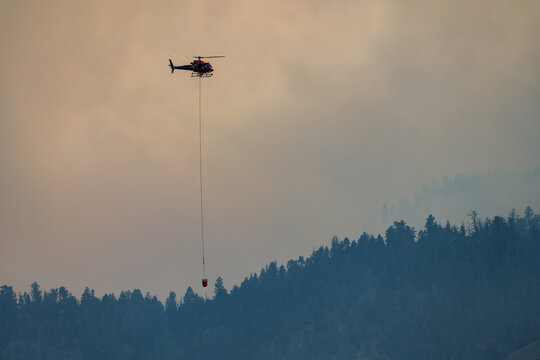 Firefighting helicopter with water bucket over smoky forest