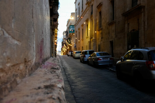 Parked cars lining narrow street with festive string lights in valletta, malta