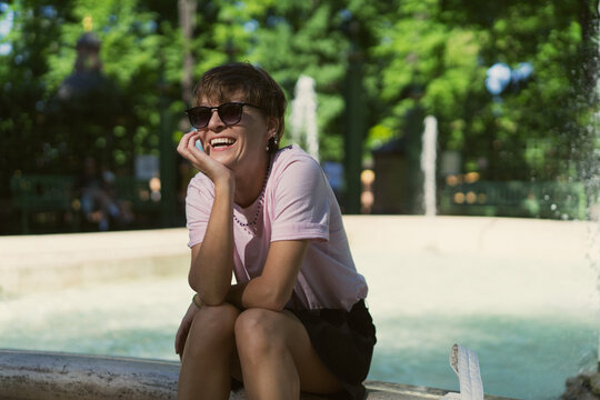 Happy young woman laughing by a park fountain in Summer Garden