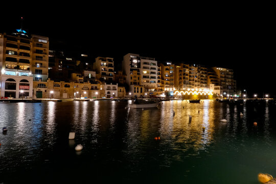 Spinola bay, st. Julian's, malta at night showing illuminated buildings and boats