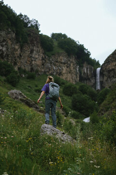 Woman with backpack hiking toward a waterfall in the mountains