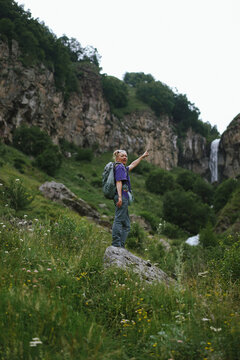 Woman with backpack points toward mountain waterfall