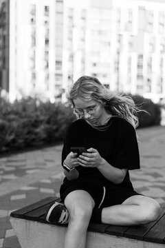 Teenage girl with windy hair uses phone on bench