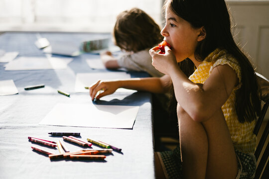 Young girl eats a snack while drawing at a table