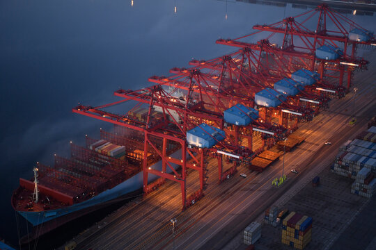 A container ship is loaded with cargo containers at port cranes