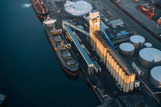 A cargo ship docked at an industrial port next to grain silos in Long