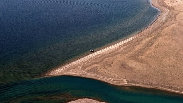 Aerial view of the shoreline of Twin Lakes, showing the contrast between the deep blue water and the sandy beach, with a small boat near the edge in Twin Lakes, Colorado, United States.