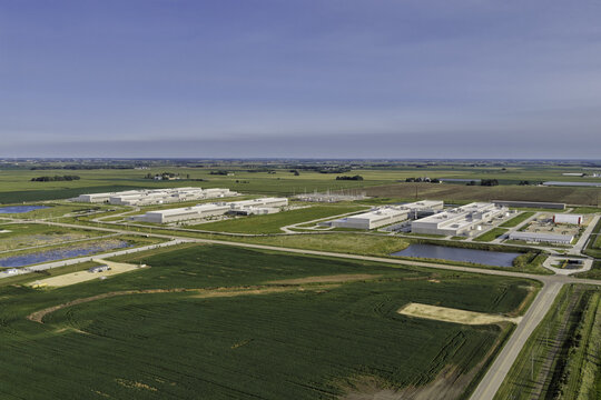 Aerial view of the Meta data center complex surrounded by vast agricultural fields and green farmland under a clear blue sky in DeKalb, Illinois, United States.