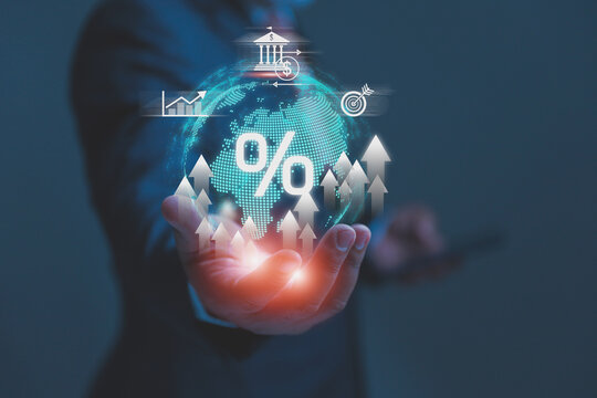 A professional businessman holds a glowing digital globe icon in the palm of his hand, with a percentage symbol highlighting global interest rates, inflation, and financial growth.
