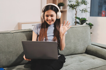 Beautiful young asian woman sitting on sofa and holding joystick playing online video game in living room at house © ARMMY PICCA