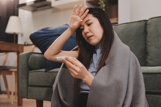 sick asian young woman sneezing into tissue paper while covered with a blanket and sitting on sofa in the living room