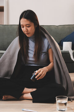 sick asian young woman sneezing into tissue paper while covered with a blanket and sitting on sofa in the living room