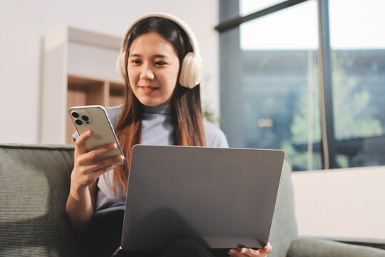 Beautiful young asian woman sitting on sofa and holding joystick playing online video game in living room at house