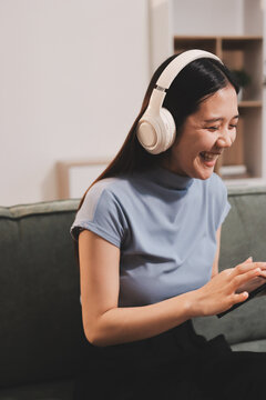 Freelance Asian woman holding mobile phone typing on laptop and working from home. Happy young girl sitting on sofa in living room.
