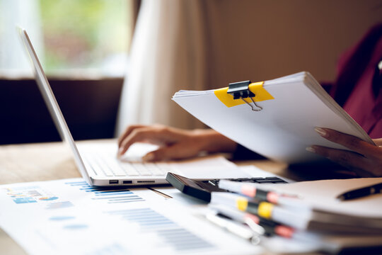 Business professional working on a laptop with financial charts, calculator, documents and coffee on a wooden desk, representing finance, accounting and office work.