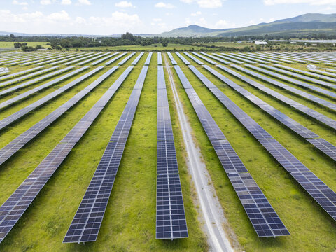 Aerial view of a large solar farm with rows of photovoltaic panels arranged in a green field under a clear sky in Santiago de Queretaro, Queretaro, Mexico.