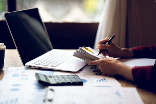 Business professional working on a laptop with financial charts, calculator, documents and coffee on a wooden desk, representing finance, accounting and office work.