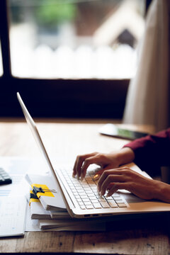 Business professional working on a laptop with financial charts, calculator, documents and coffee on a wooden desk, representing finance, accounting and office work.