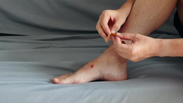 Person applies a protective adhesive bandage to a small red skin wound on the top of the foot