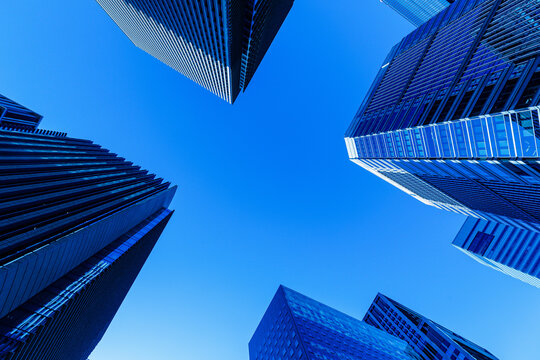 Direct vertical worm's-eye view looking up at modern glass skyscrapers surrounding clear blue sky copyspace in Tokyo.