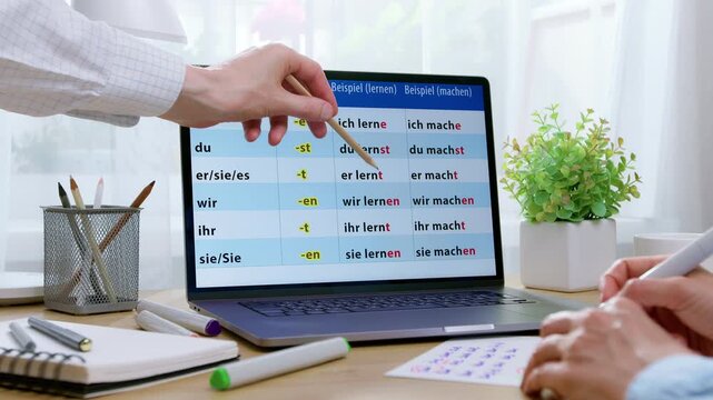 Close-up of people pointing with a pencil at German grammar words on a laptop screen at a work desk. The interactive lesson focuses on online foreign language study. Education concept.