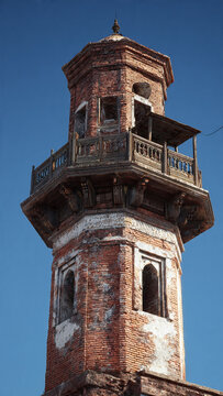 A tall, old, red brick tower with a balcony and a clear blue sky in the background