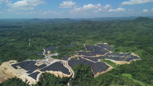 High-altitude drone slides left and orbits the hillside solar arrays and access roads of Sikatuna Solar Power Plant in Bohol