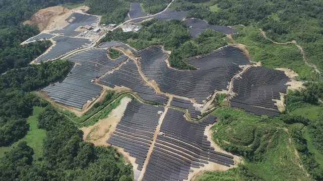 Drone flies over and tilts down across hillside solar panel arrays, access roads, and surrounding forest at Sikatuna Solar Power Plant